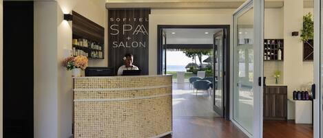 A reception area with a reception desk, a sign for a spa and salon, a large chandelier, and a view of the outdoors.