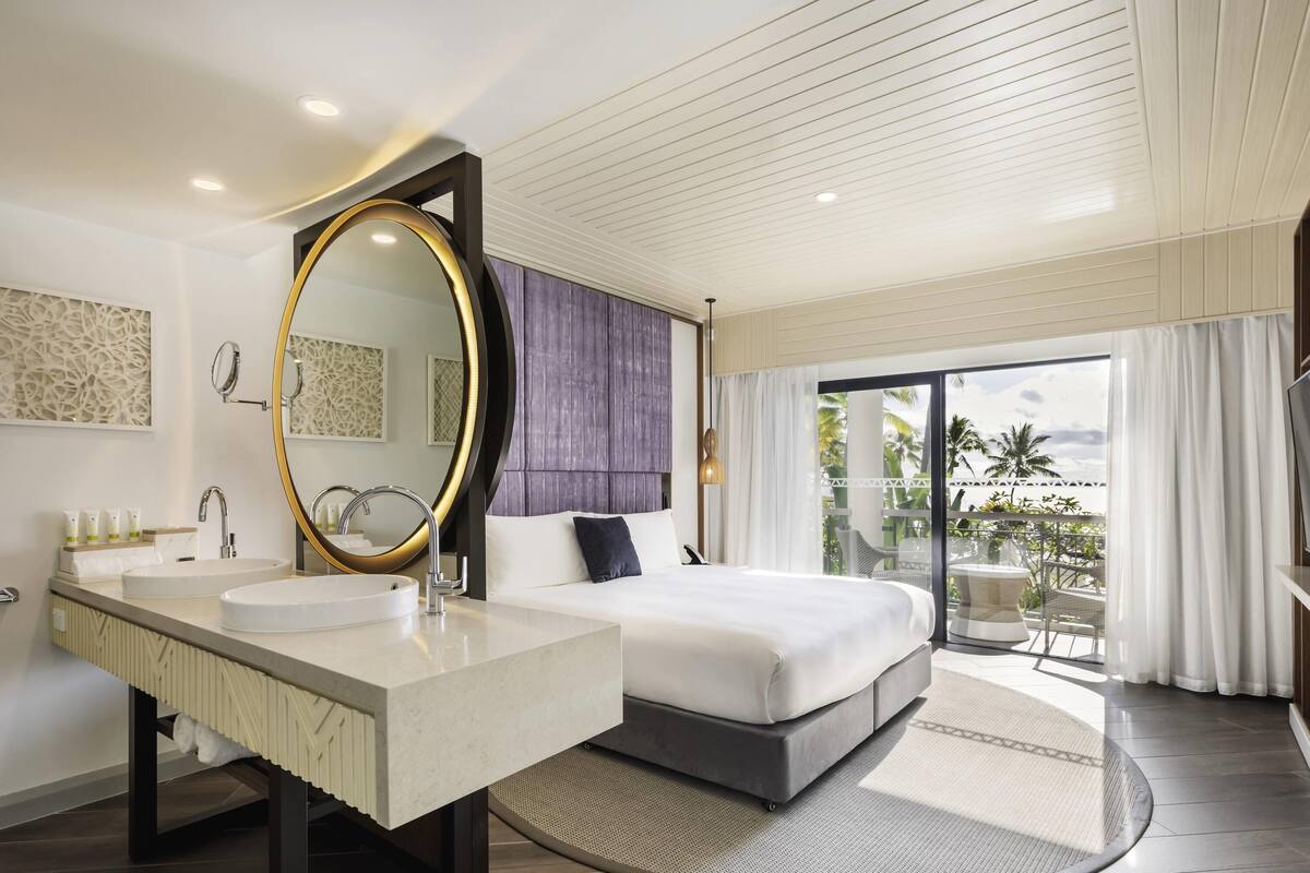 Une chambre d’hôtel moderne dotée d’un grand lit, d’un miroir rond, d’un lavabo double et d’un balcon avec vue.