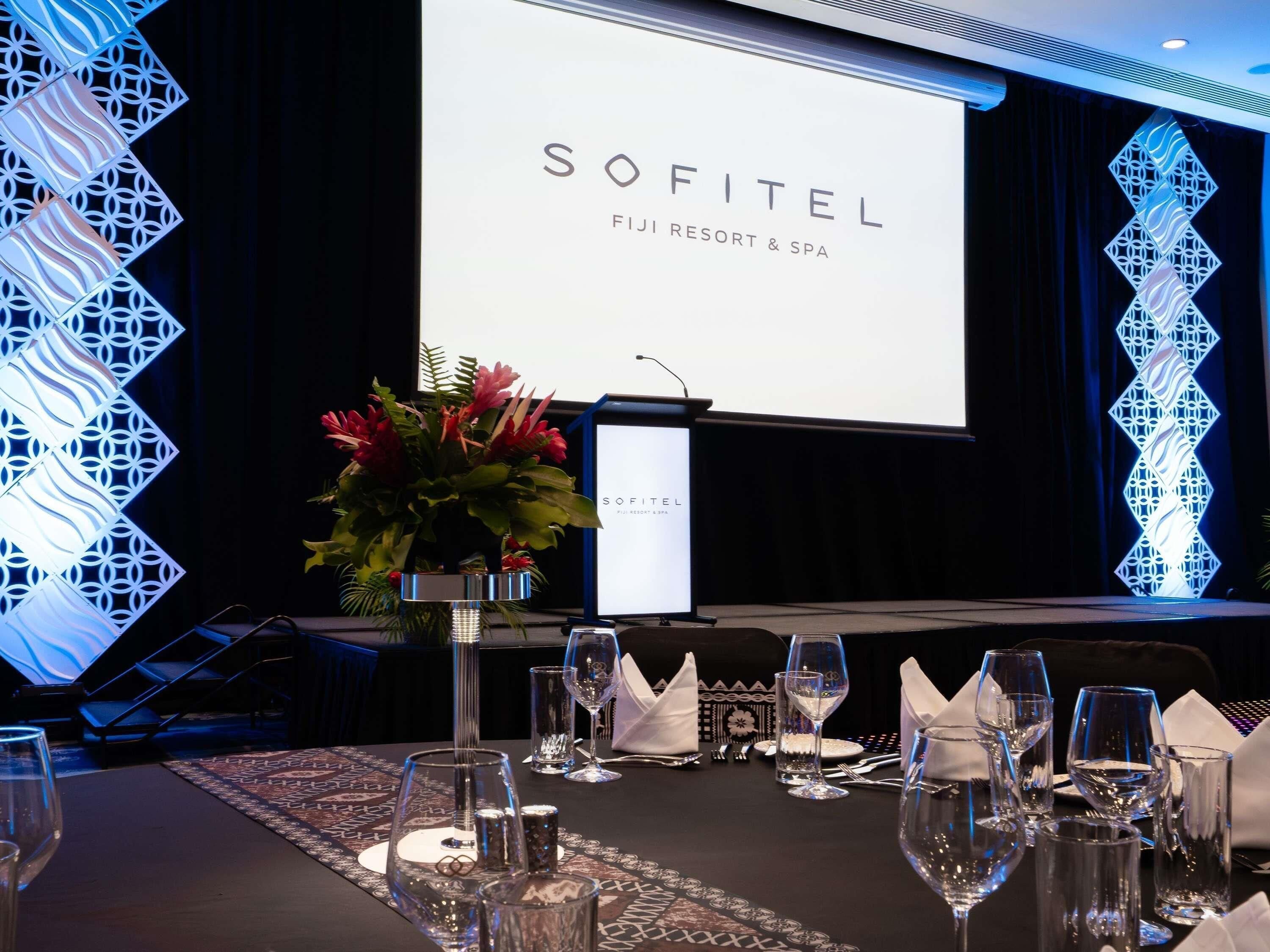 A conference room with a presentation screen, a floral centerpiece, and a table set for a meeting.