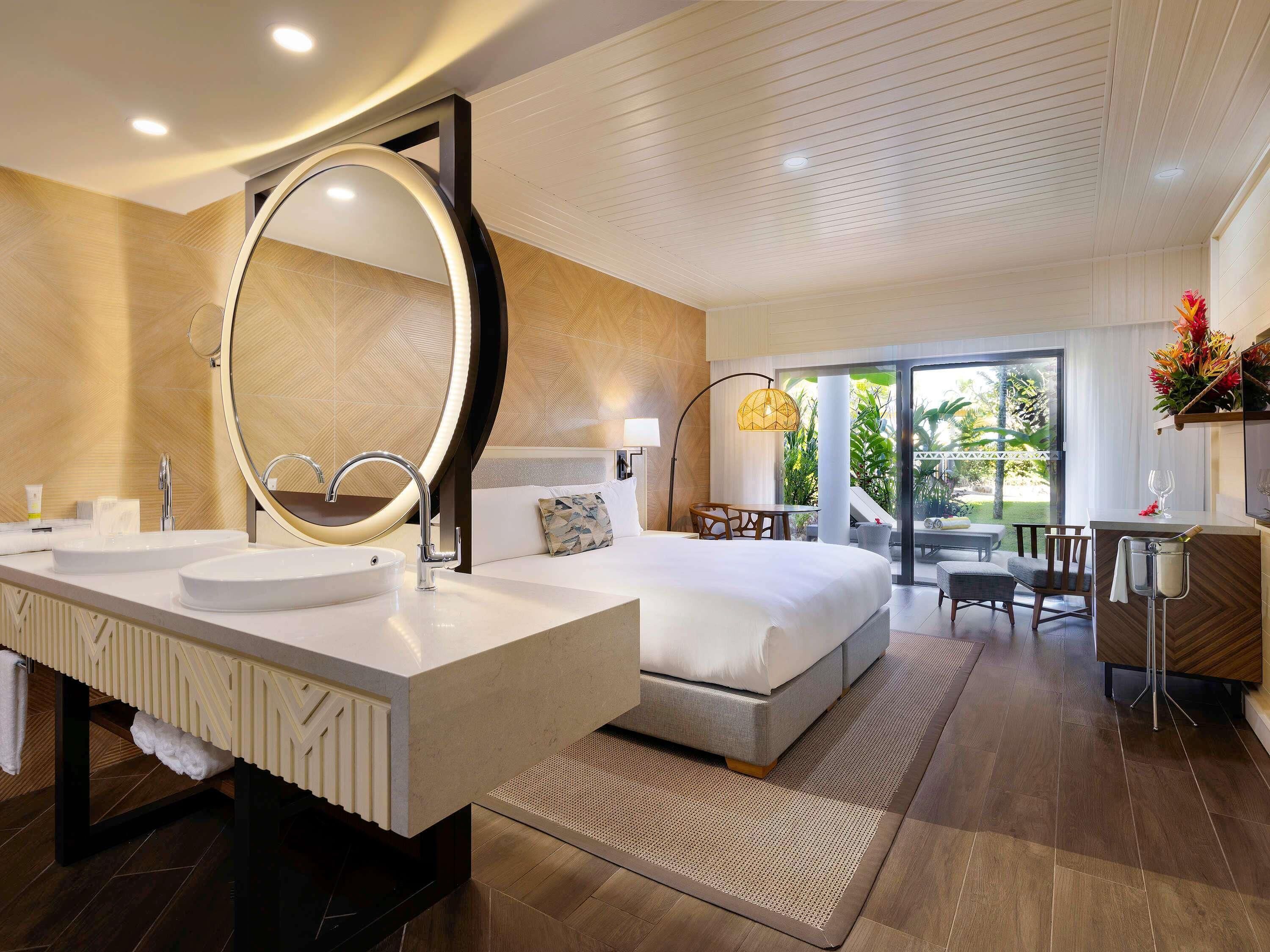 A modern hotel room with a large bed, two sinks, a large mirror, and a balcony with a view.