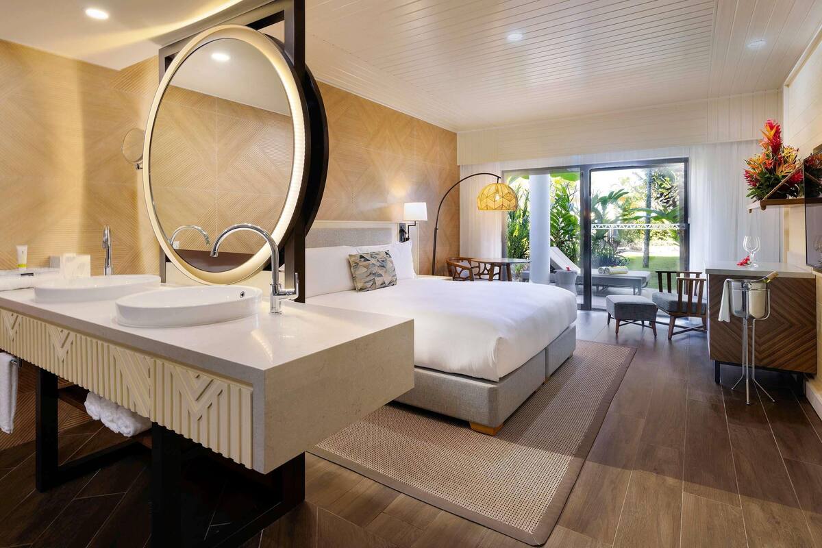 Une chambre d’hôtel moderne avec un grand lit, deux lavabos, un grand miroir et un balcon avec vue.