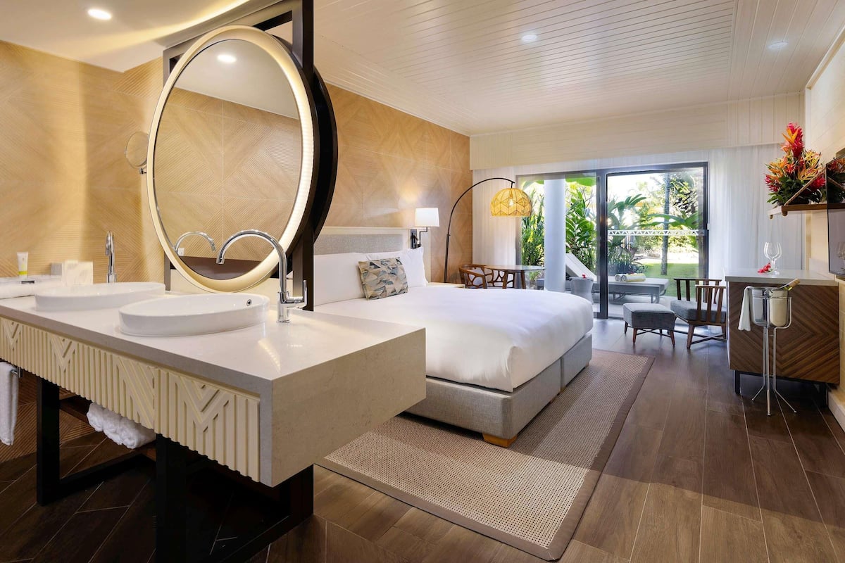A modern hotel room with a large bed, two sinks, a large mirror, and a balcony with a view.