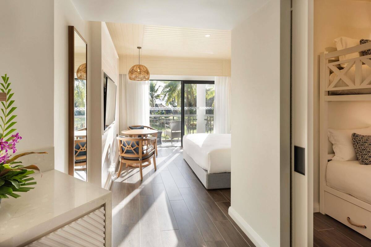Une chambre d’hôtel avec un lit, une petite table avec des chaises, un balcon avec vue et un plancher en bois.