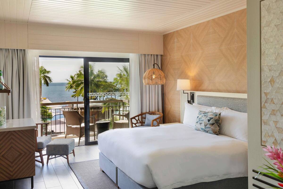 Une chambre d’hôtel comprenant un lit, un bureau, une chaise, un balcon avec vue sur la mer et un mur décoré de motifs.
