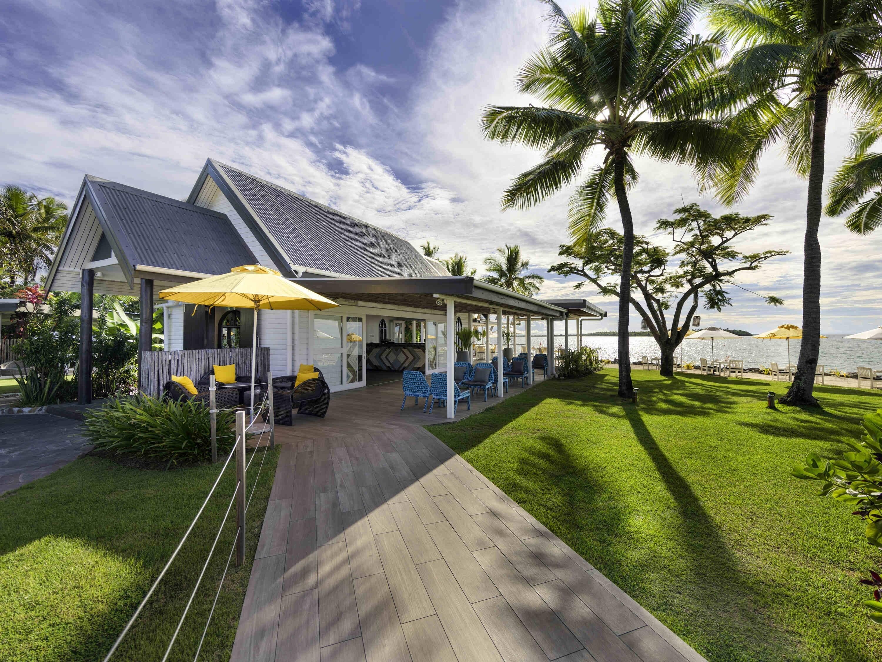 Un espace extérieur abrité, avec des chaises et des parasols, une terrasse en bois et une vue sur la mer.