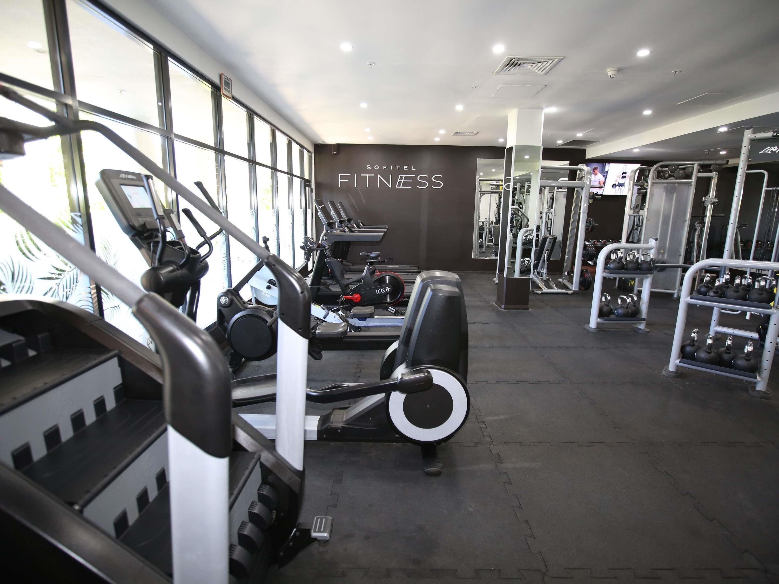 Un gimnasio con máquinas de cardio, equipo de levantamiento de pesas y una pared con el texto 'SOFTEL FITNESS'.
