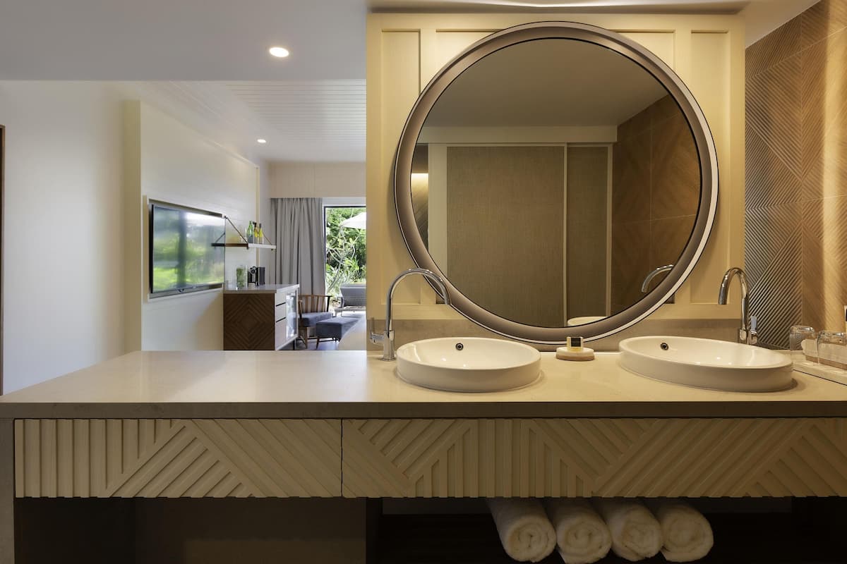 A modern bathroom with two sinks, a large mirror, and a view of a balcony with a dining area.