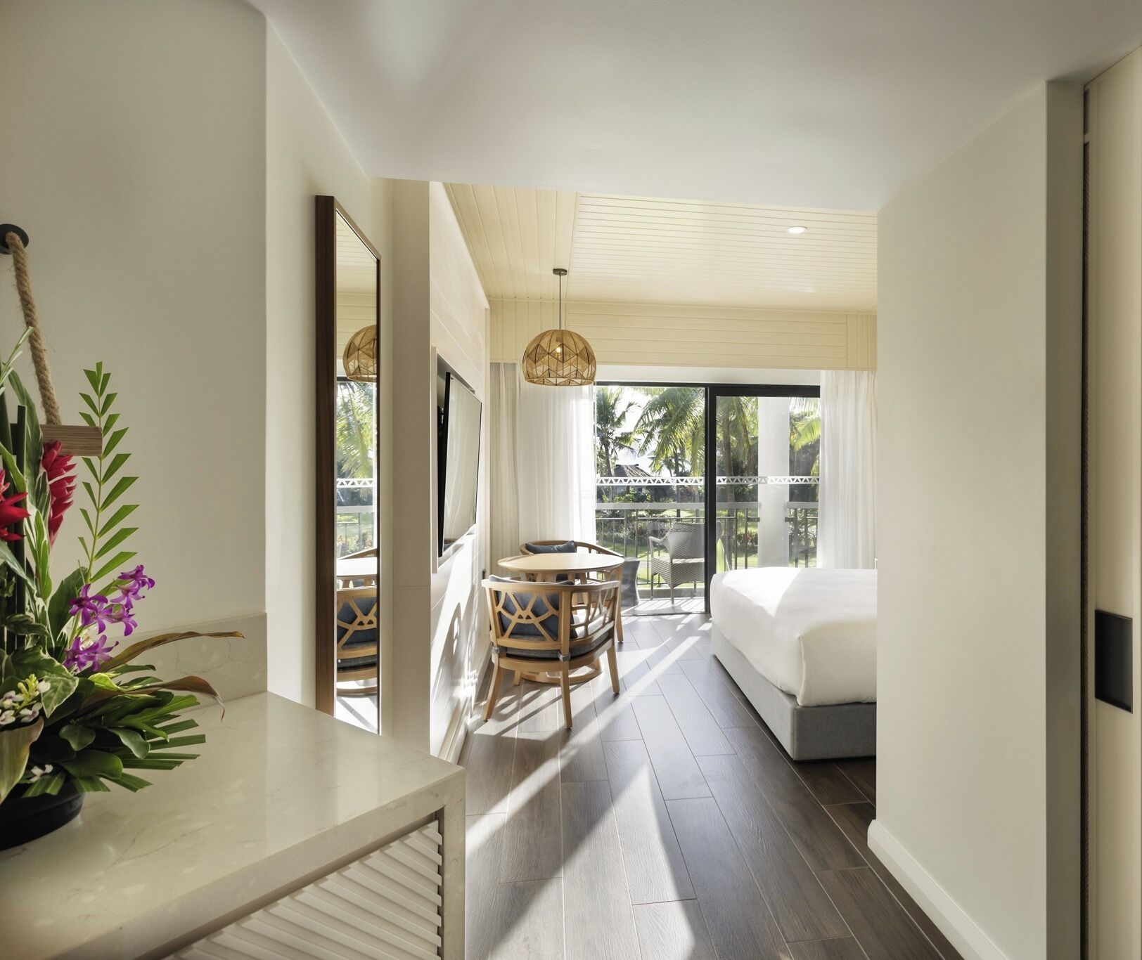 A modern hotel room with a balcony, a dining area with a table and chairs, and a large bed.