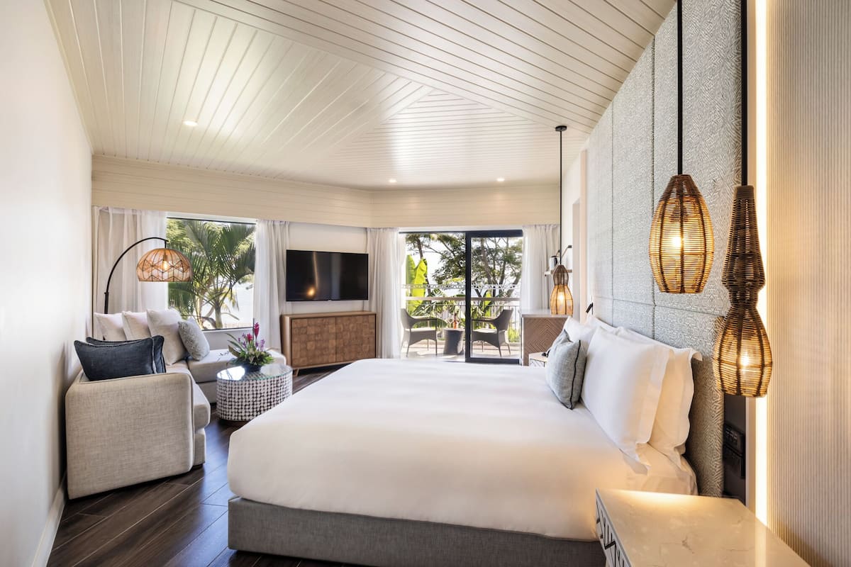 Une chambre d’hôtel moderne dotée d’un grand lit, d’un canapé, d’une télévision et d’un balcon avec coin salon extérieur.