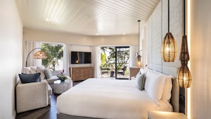 A modern hotel room with a large bed, a sofa, a TV, and a balcony with outdoor seating.