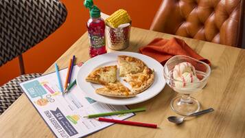 A table with a pizza, a bowl of ice cream, a menu, and a bottle of fruit juice.