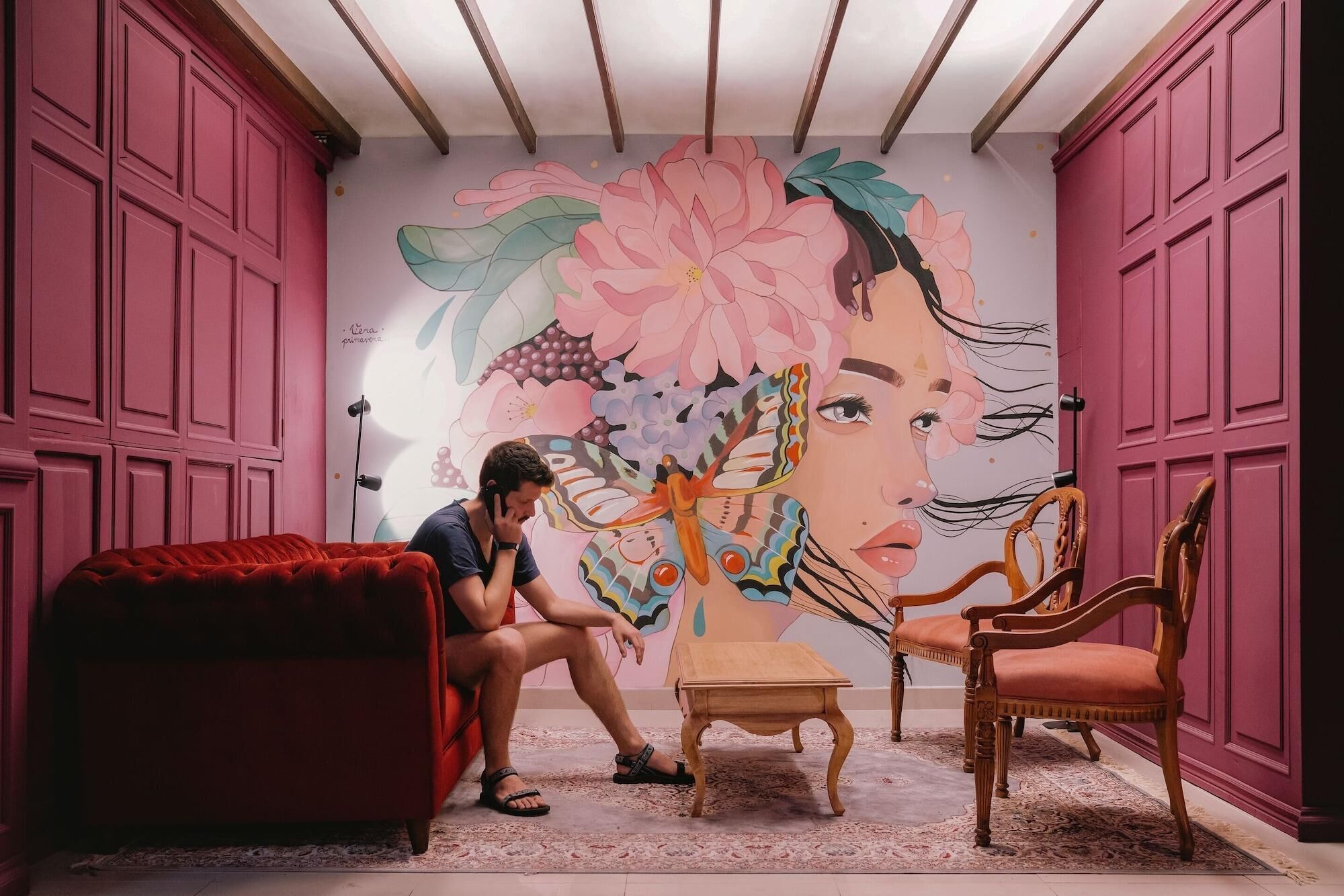Una habitación con un gran mural floral, un sofá rojo, una mesa de madera y dos sillas de madera.