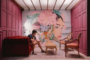 Una habitación con un gran mural floral, un sofá rojo, una mesa de madera y dos sillas de madera.