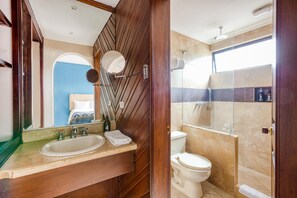 Un baño con tocador de madera, lavamanos, espejo, inodoro y zona de ducha.
