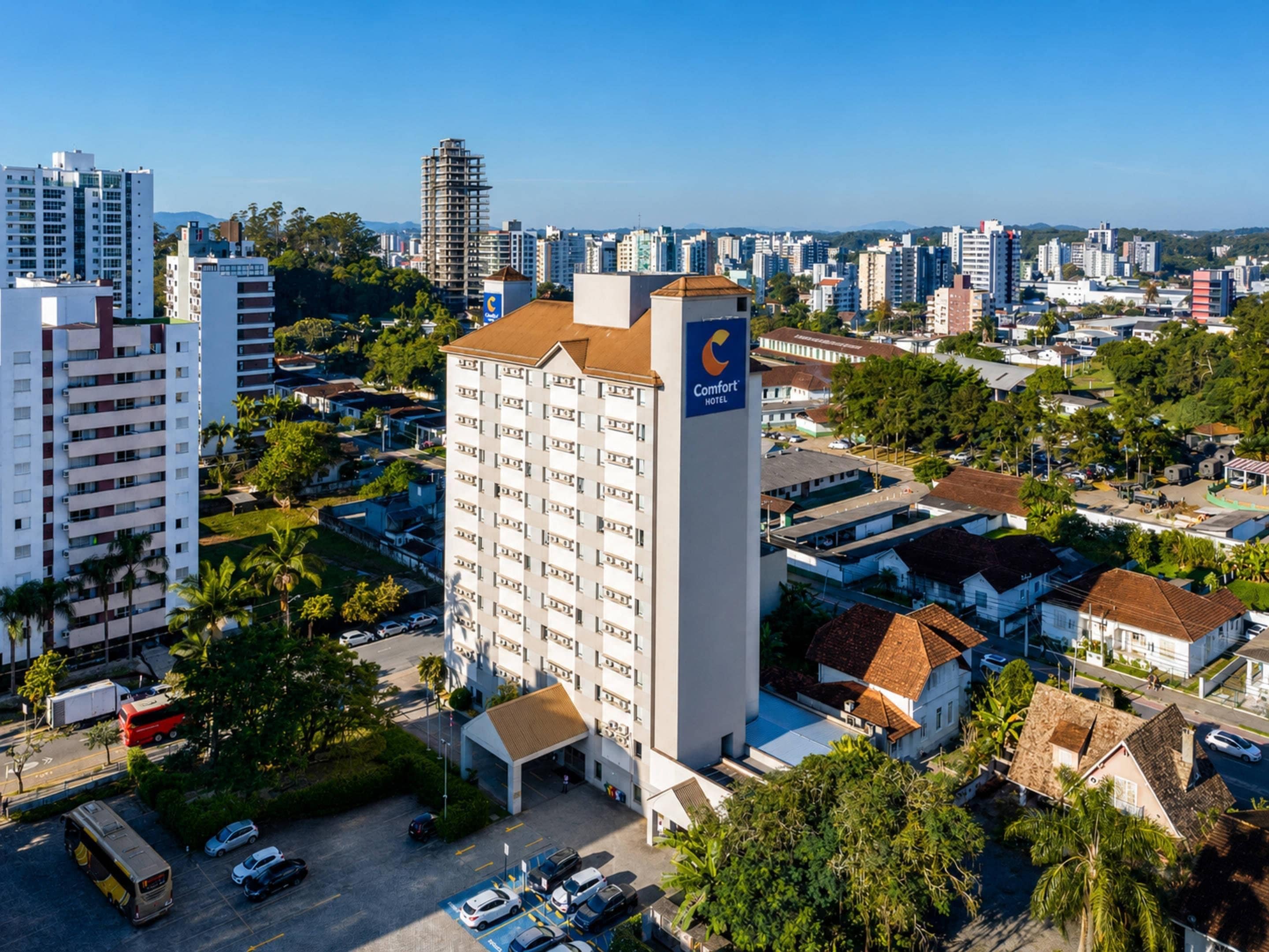 Un hotel de varios pisos con un letrero llamativo, rodeado de edificios residenciales y vegetación.
