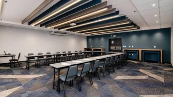 Een vergaderzaal met meerdere tafels en stoelen, een plafond met lineaire verlichting en een vloerbedekking.