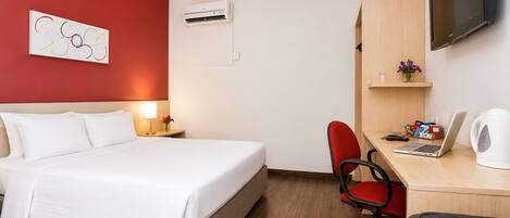A hotel room with a bed, a desk, a chair, a television, and an air conditioning unit.