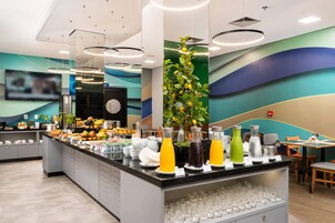 Um balcão de café da manhã moderno com diversas opções de alimentos e bebidas, uma TV de tela plana e uma planta decorativa.