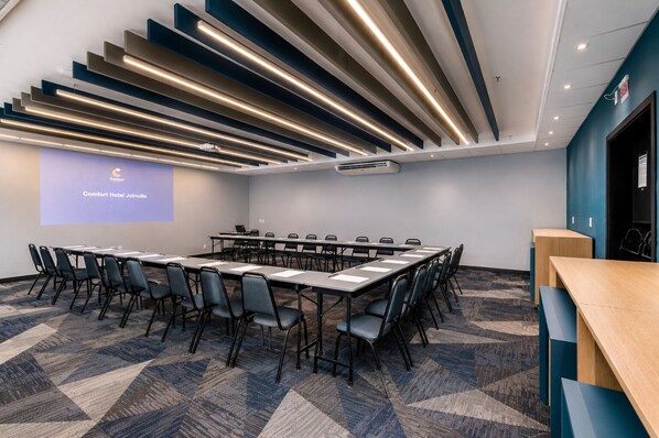 A conference room with a long table, chairs, a projector screen, and a modern ceiling design. - Comfort Hotel Joinville (Joinville)