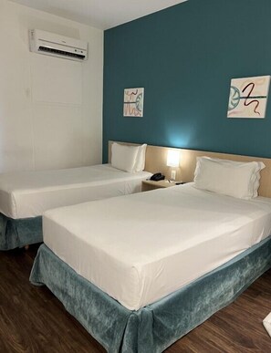 A hotel room with two single beds, a nightstand with a lamp, and an air conditioning unit on the wall. - Comfort Hotel Joinville (Joinville)