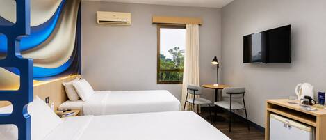 Habitación de hotel con dos camas, un escritorio con silla, televisor y ventana con cortinas.
