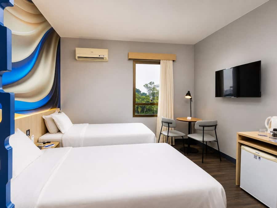 Ein Hotelzimmer mit zwei Betten, einem Schreibtisch mit Stuhl, einem Fernseher und einem Fenster mit Vorhängen.