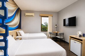 Habitación de hotel con dos camas, un escritorio con silla, televisor y ventana con cortinas.