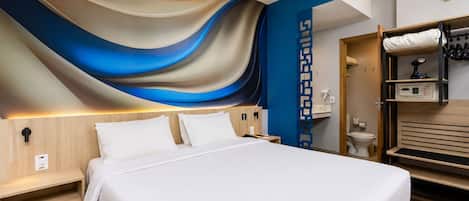 Ein modernes Hotelzimmer mit einem großen Bett, einem Holzkopfende, einer eingebauten Garderobe und einer Wand mit einem blauen und beigefarbenen abstrakten Muster.