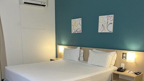 A neatly made bed with white linens, a teal accent wall, and a wooden floor. - Comfort Hotel Joinville (Joinville)