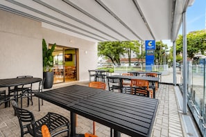 Un patio al aire libre con mesas y sillas, una planta en maceta y vista a la calle.