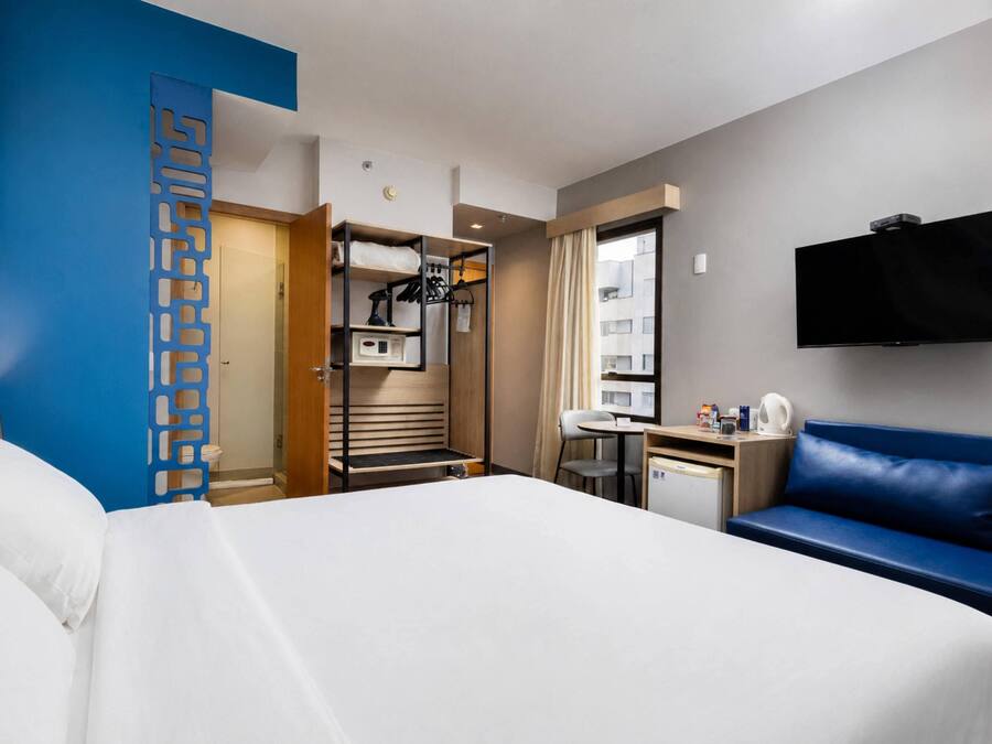 Een hotelkamer met een bed, bureau, televisie, zithoek en garderobe.