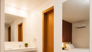 A hotel room with a bed, a mirror, a small sink, and a heater.