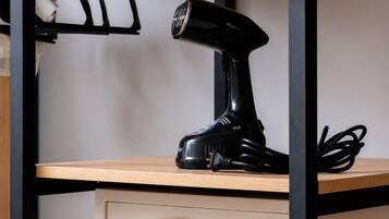 A shelf with a rolled-up towel, a black hairdryer, and a white electronic device with a keypad.