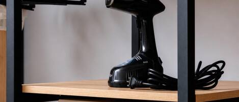 A shelf with a rolled-up towel, a black hairdryer, and a white electronic device with a keypad.