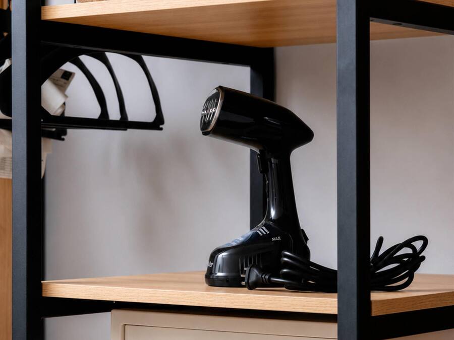 A shelf with a rolled-up towel, a black hairdryer, and a white electronic device with a keypad.