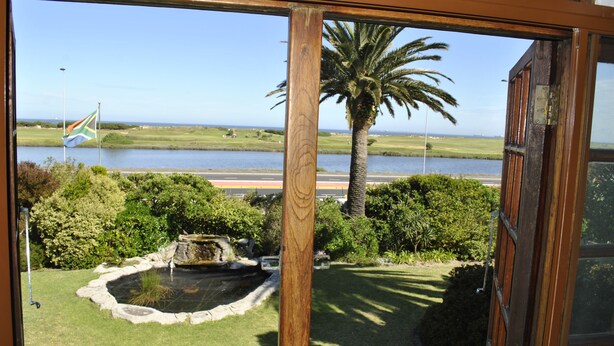 Une vue à travers une fenêtre sur un jardin aménagé, avec un étang, un palmier et un drapeau.