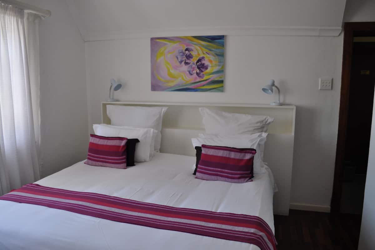 A hotel room with a large bed, white bedding, and a colorful abstract painting on the wall.