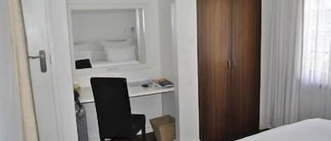 Una habitación de hotel con una cama, un escritorio con una computadora, una silla y un armario.