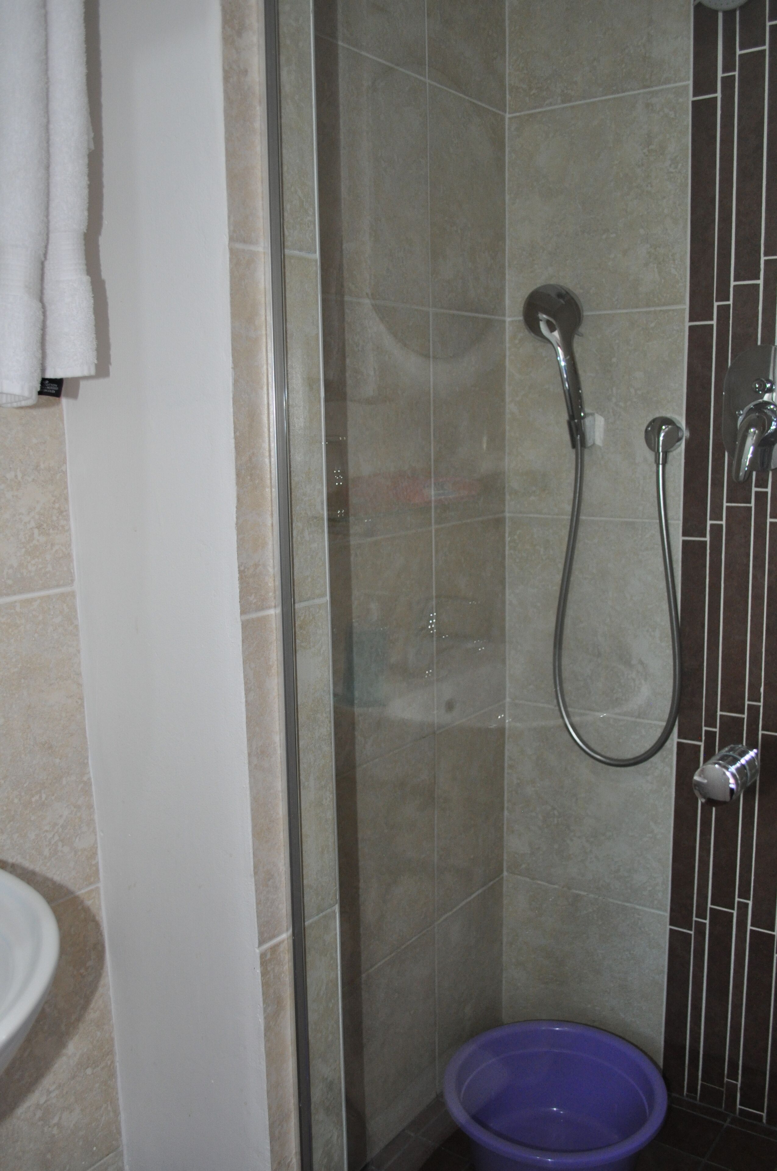 A bathroom with a glass shower enclosure, a purple basin, and a white sink.