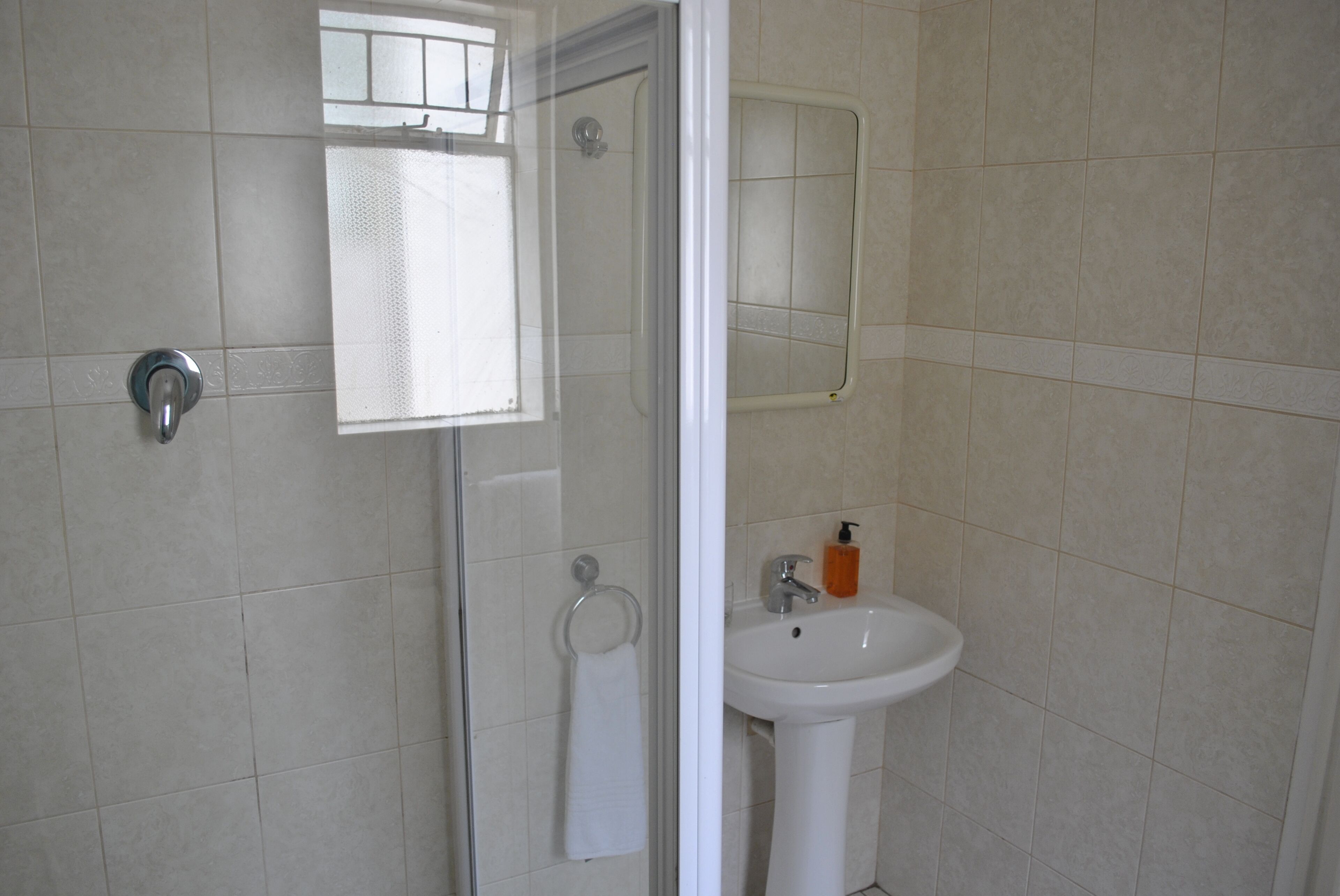 Un baño con ducha, lavamanos y perchero para toallas.