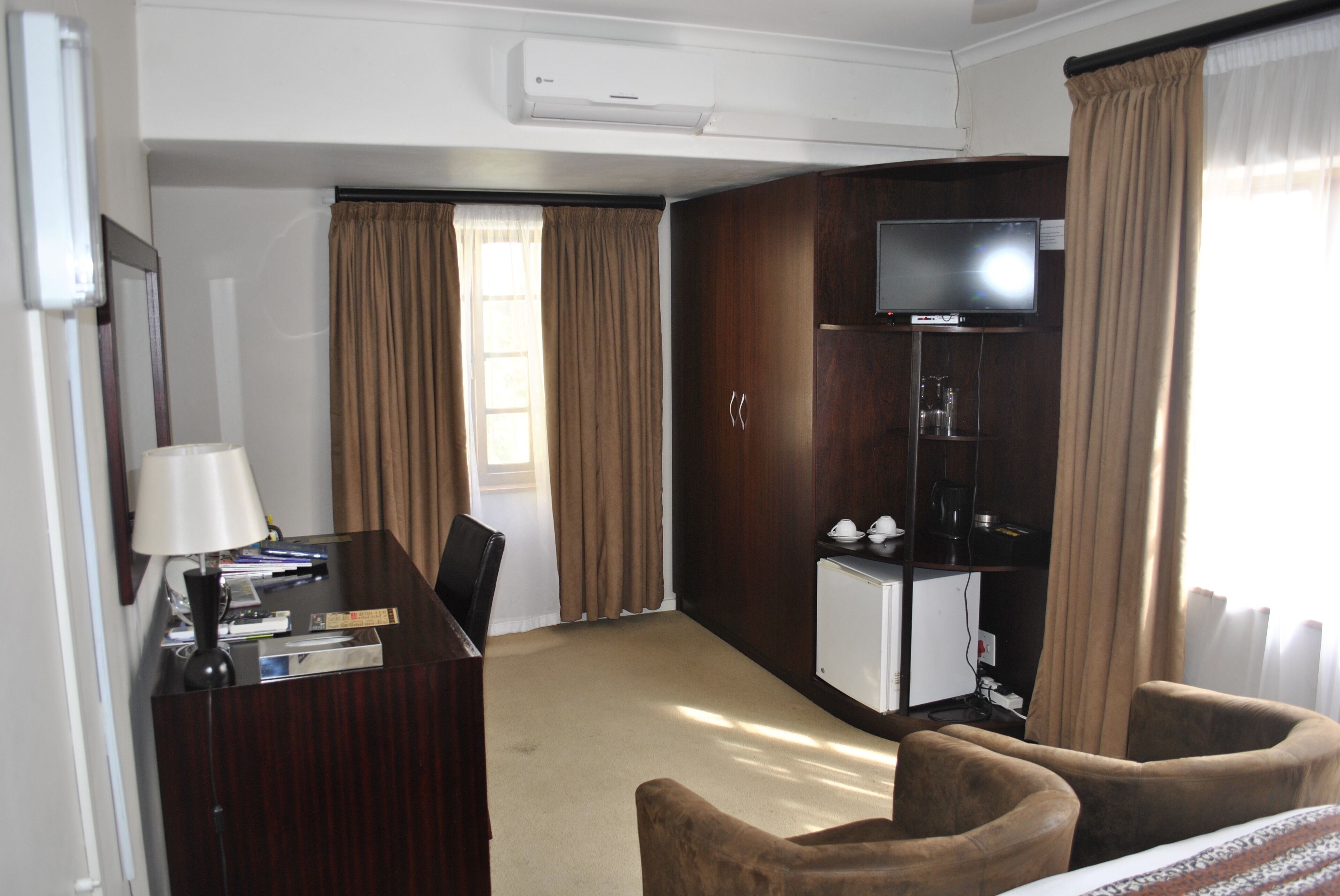 Habitación de hotel con escritorio, silla, televisor, minibar y cortinas.