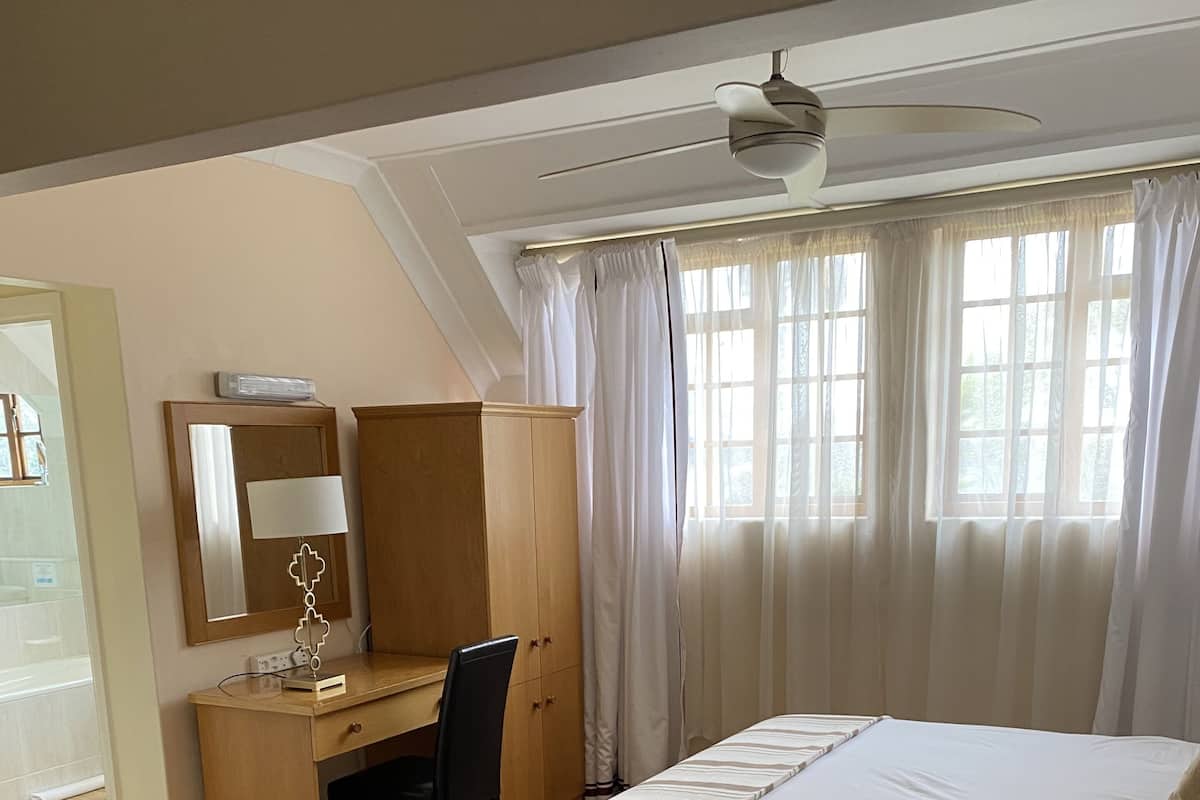A hotel room with a bed, a desk, a chair, a mirror, and a ceiling fan.