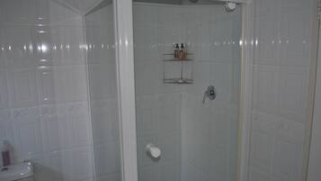 Ducha con puerta de vidrio, inodoro y estante con artículos de aseo.