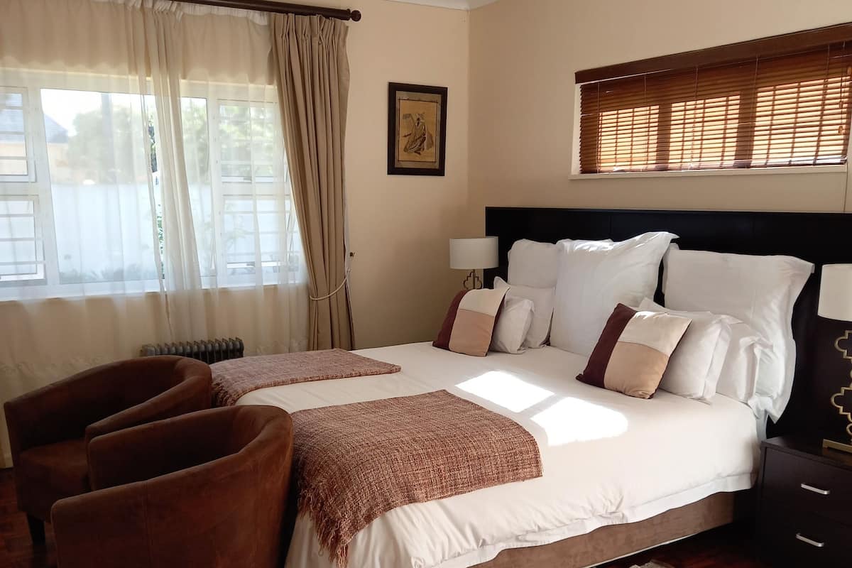 A bedroom with a bed, two armchairs, a bedside table, a lamp, and a ceiling fan.