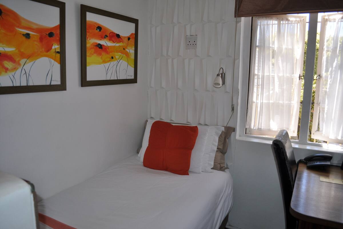 A bedroom with a bed, a desk, and two paintings on the wall.