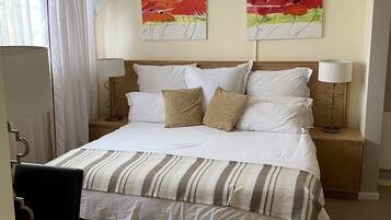 A neatly arranged hotel room with a bed, bedside lamps, a ceiling fan, and two wall-mounted air conditioning units.