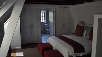 Quarto com cama grande, manta vermelha e vista para um banheiro através de uma porta aberta.