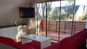 Un salon moderne avec un téléviseur à écran plat, un canapé blanc, un coussin rouge et un bol décoratif.