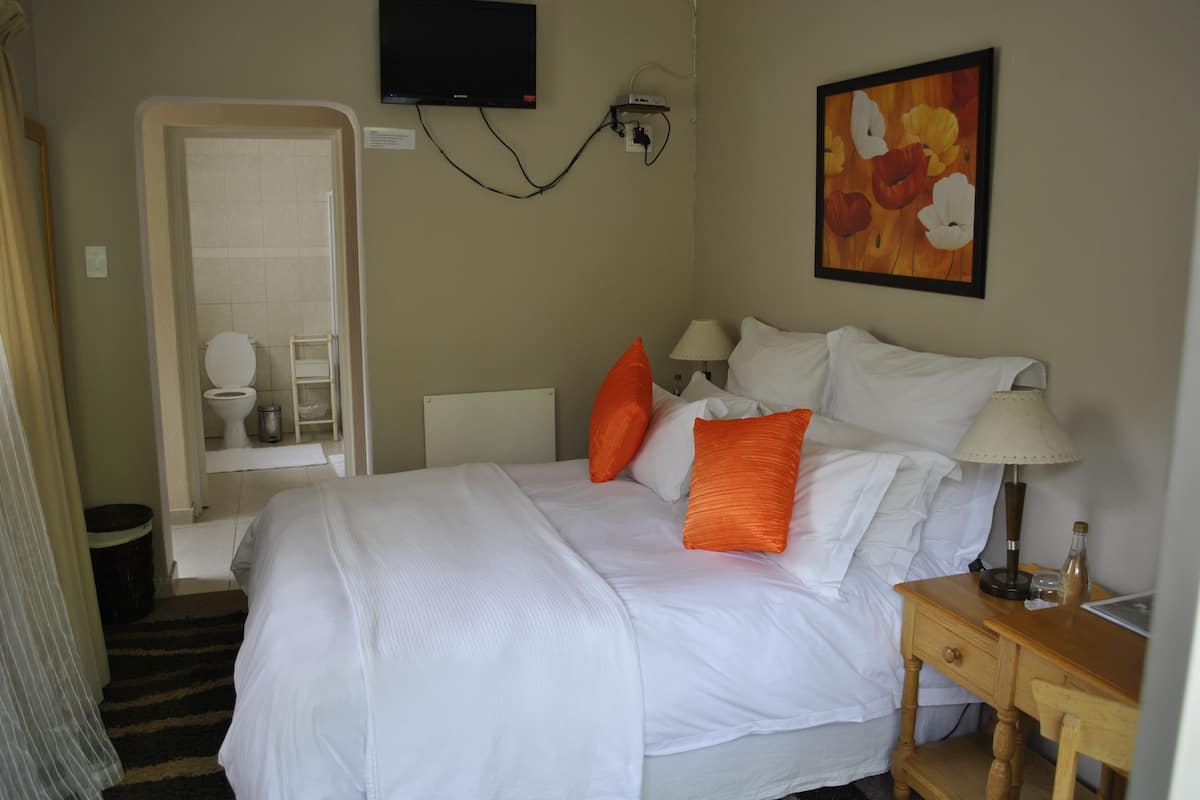 A hotel room with a bed, pillows, a bedside table, a lamp, a TV, and a painting on the wall.