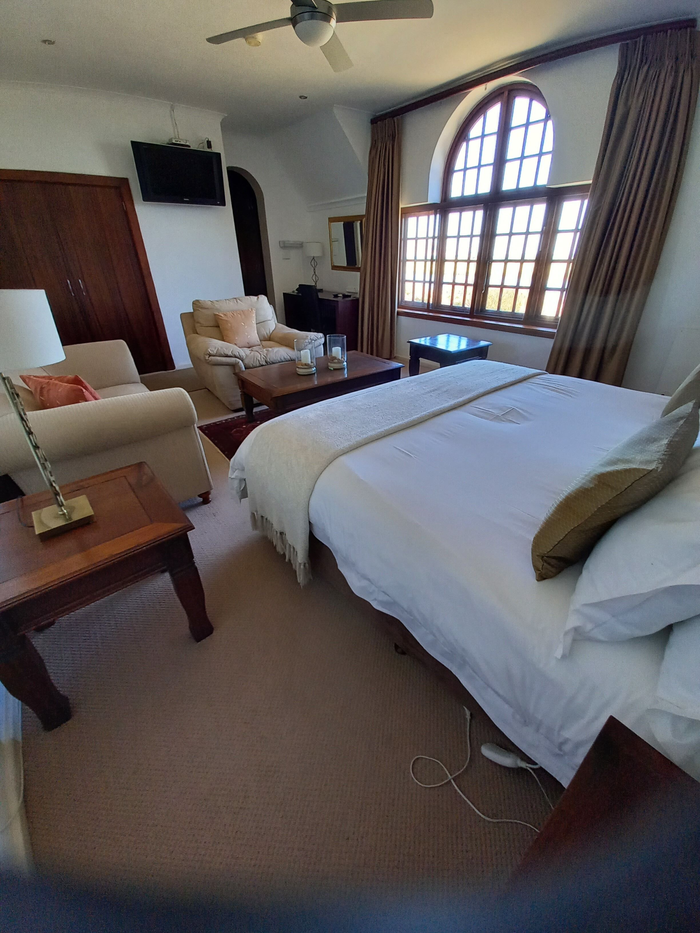 A hotel room with a bed, a sofa, a desk, a television, and a window with curtains.